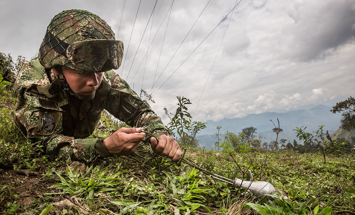 A soldier bending over to remove an antipersonnel mine.