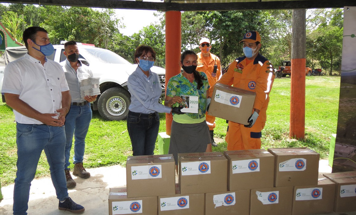 A woman shows the humanitarian aid package next to a TGI employee and a Civil Defense member.