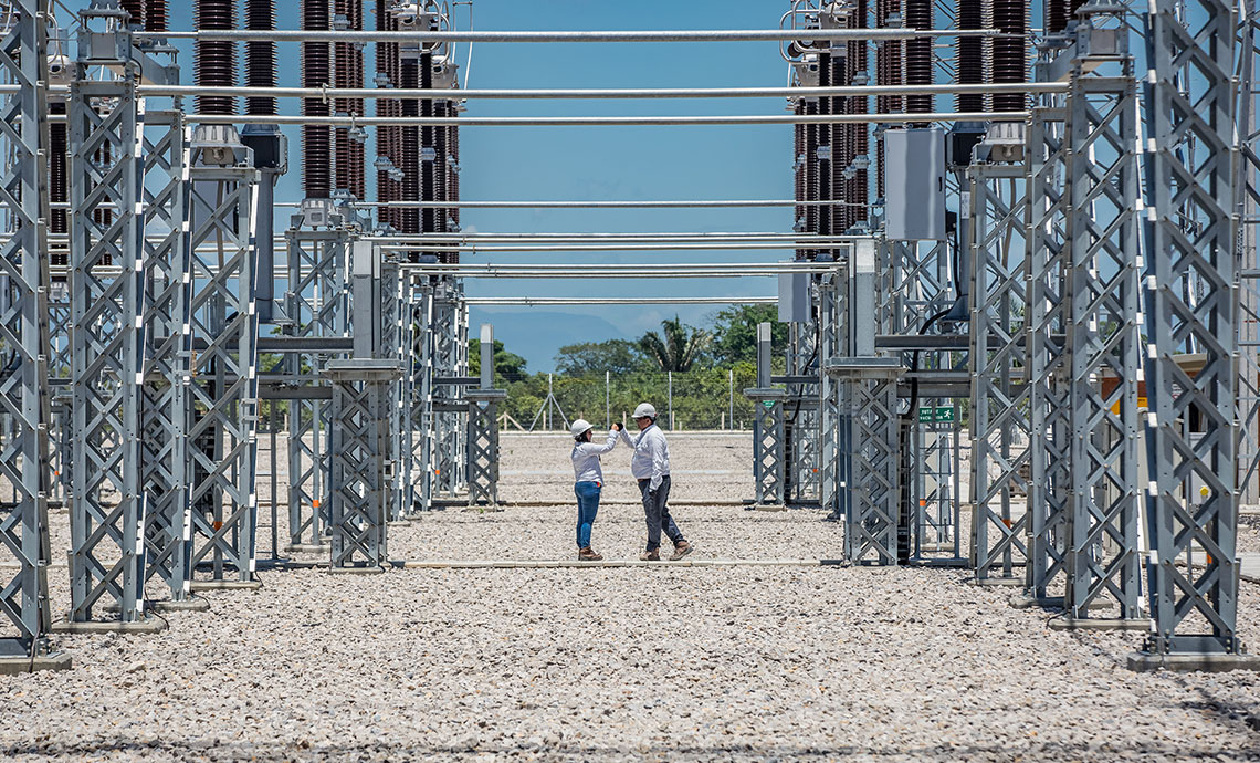 Dos operarios chocan sus puños en medio de la infraestructura de la operación al aire libre.