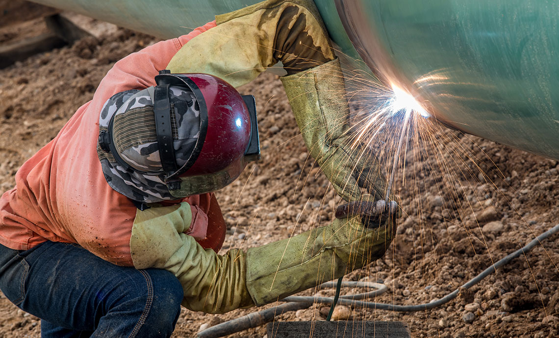 Operator bending over to weld thick pipe.
