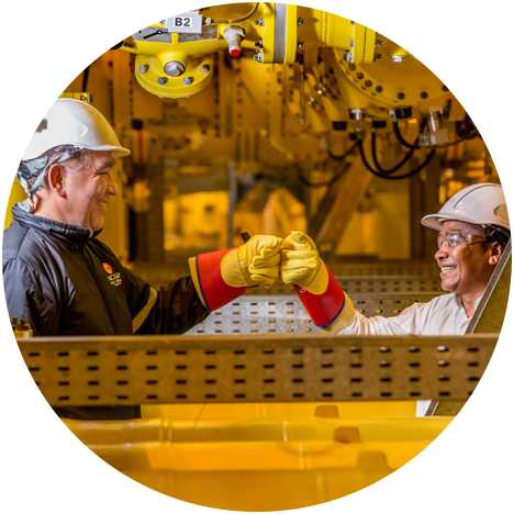 A male and a female worker bump fists and smile at their workstation.
