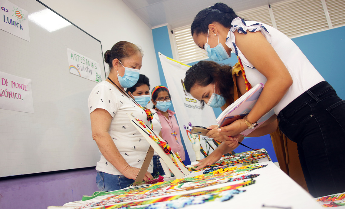 mujeres artesanas exhiben sus artesanías a otras mujeres.