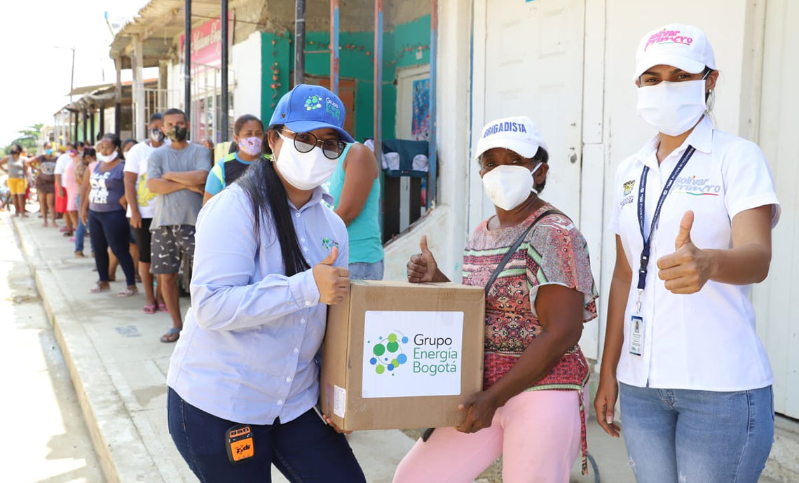 Three women wearing face masks with thumbs up hold a box labeled with the name GEB.