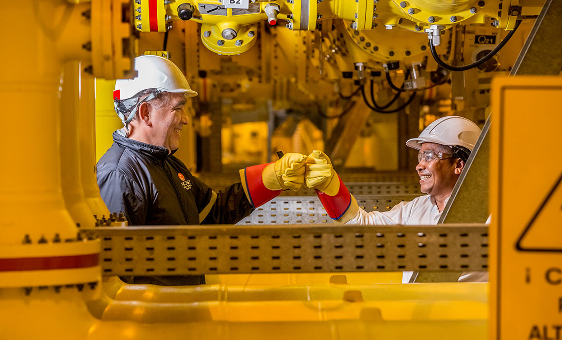 A male and a female worker bump fists and smile at their workstation.